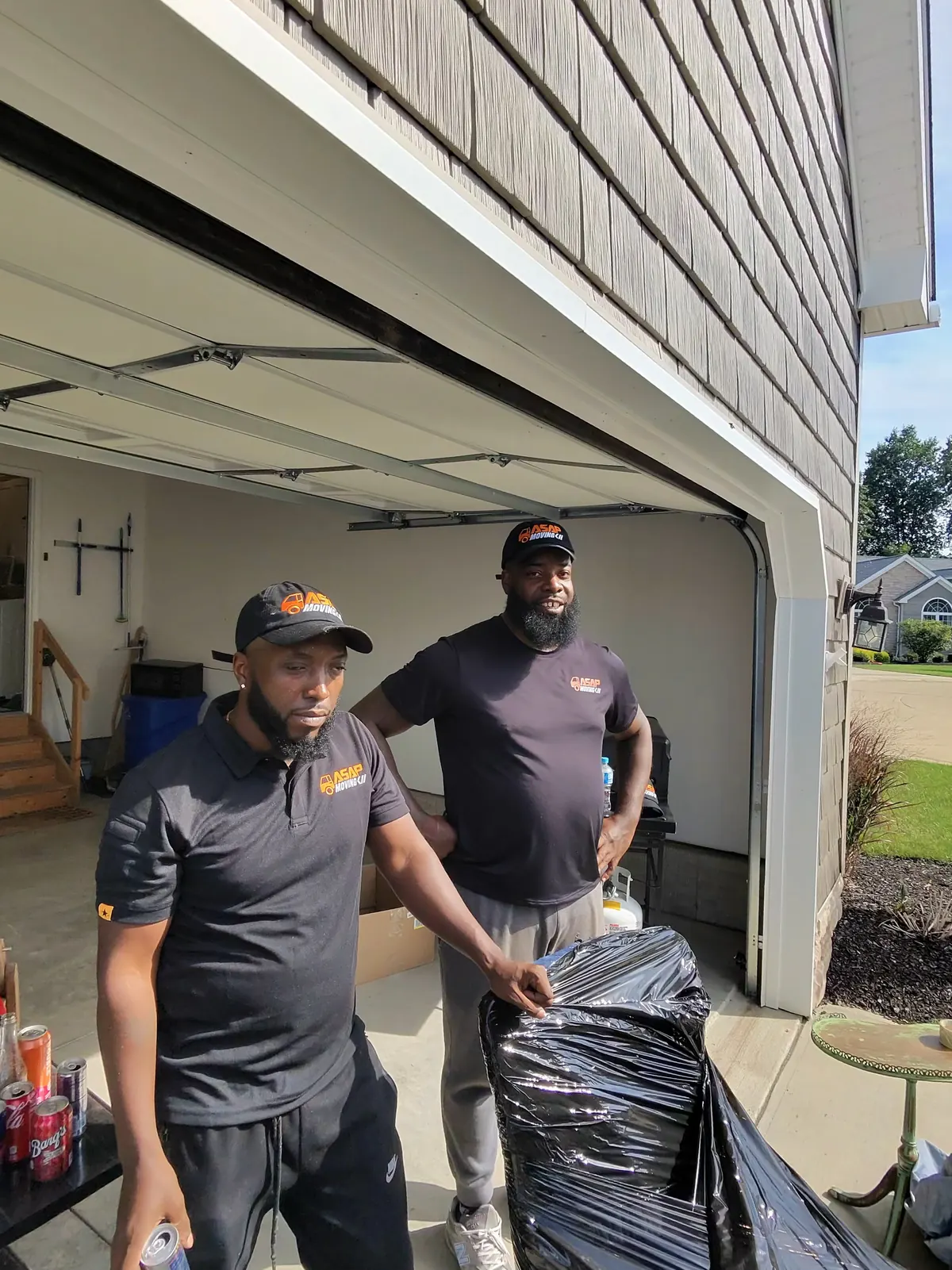 Two ASAP Moving crew members standing beside wrapped items at an open garage in Vermilion, Ohio.